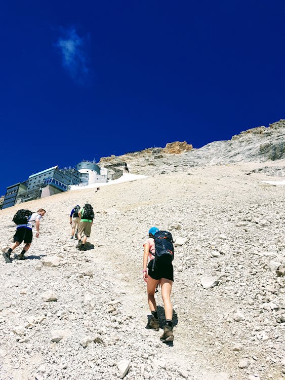 Group of four tourists with backpacks ascending a rocky mountain trail on a clear day