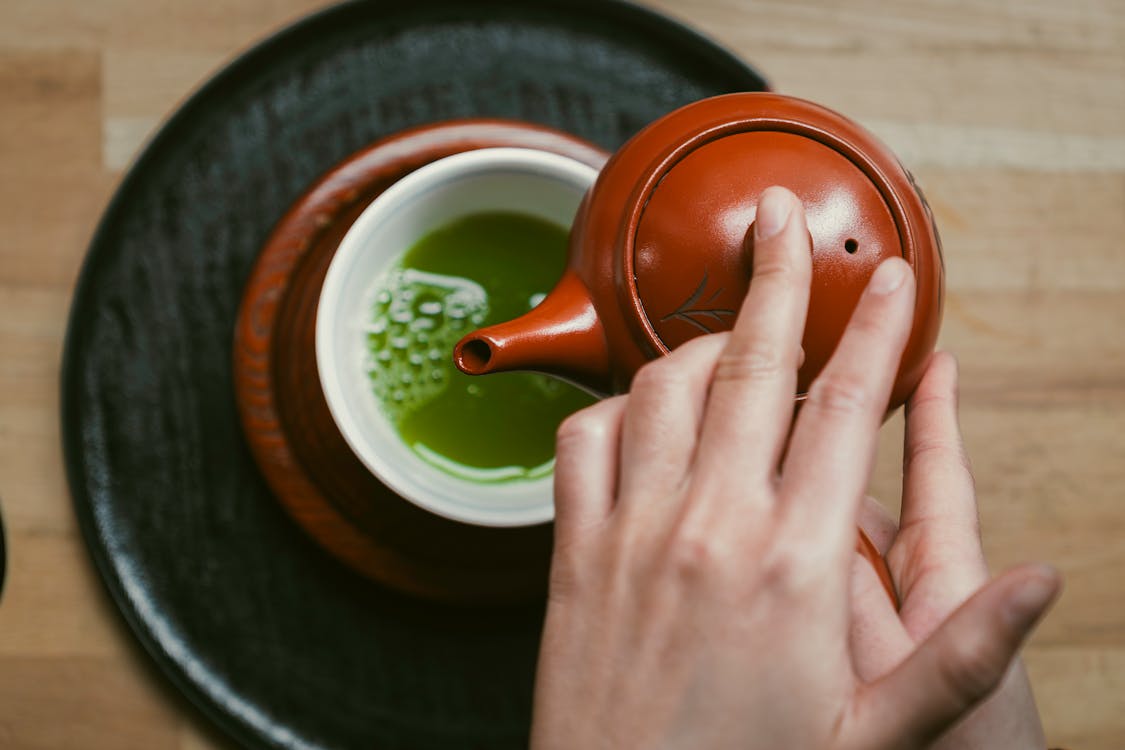 Close-up of hands carefully pouring matcha tea into a bowl during a traditional Japanese tea ceremony