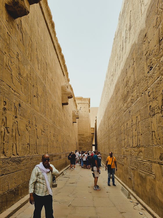 Tourists walking through an ancient Egyptian temple corridor lit by afternoon sun