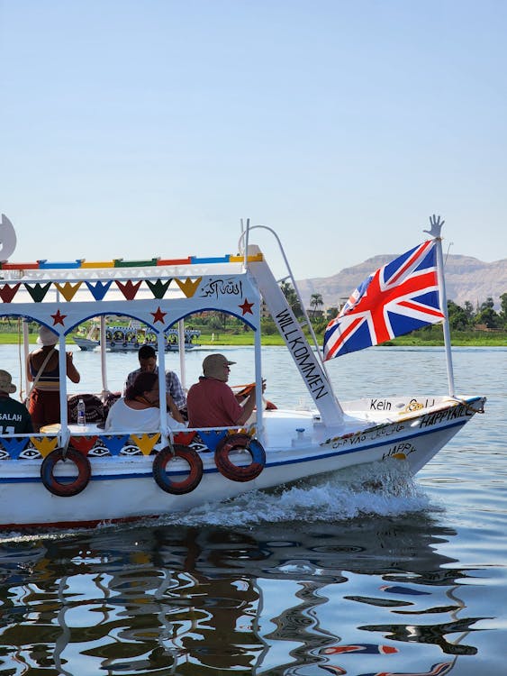 Colourful traditional Nile cruise boat with flags sailing past the Egyptian riverbank