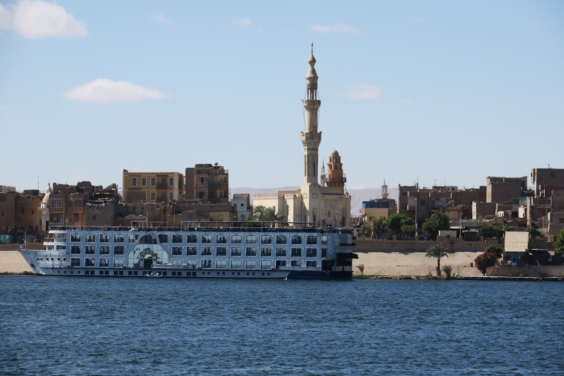 Large Nile cruise ship moored along the Aswan riverbank with a mosque dome in the background