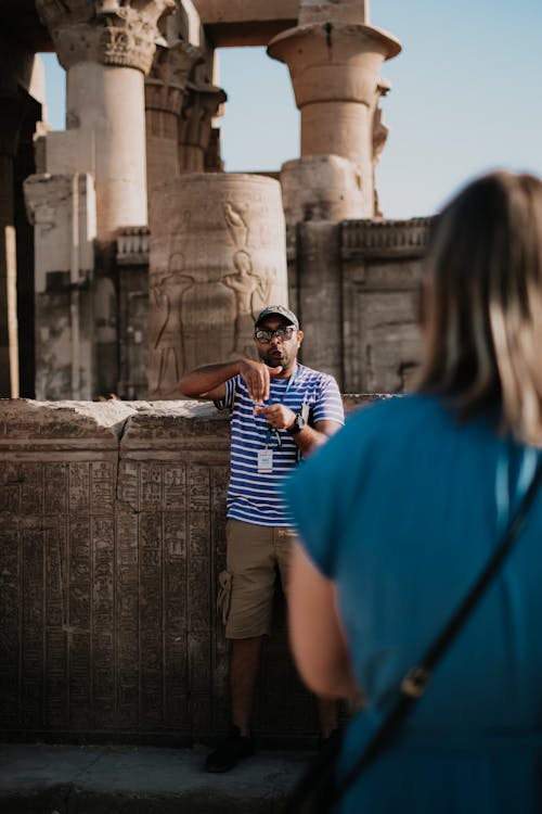 Tour guide in striped shirt explaining historical ruins at an ancient temple to a visitor