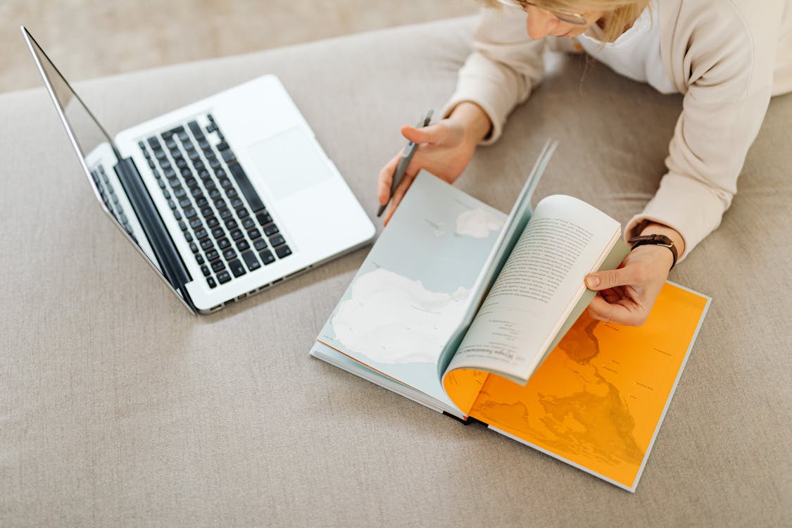 A woman using a laptop with a map and travel research materials, planning a multi-destination trip