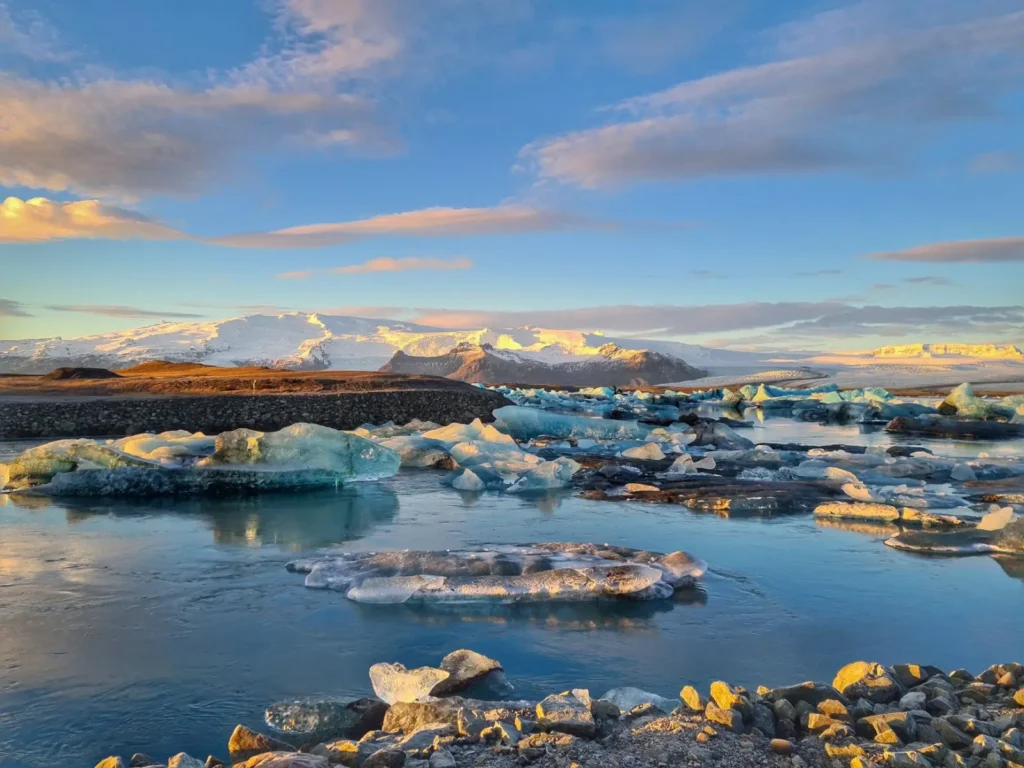 Iceland tours in June: Midnight sun, long drives, and summer touring ToursZoom A serene sunrise over Jokulsarlon glacier lagoon with golden light reflecting on the water's surface
